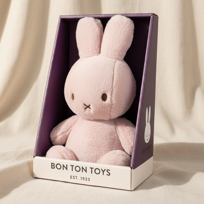 A light pink plush bunny toy in its original purple and white packaging box, branded BON TON TOYS.