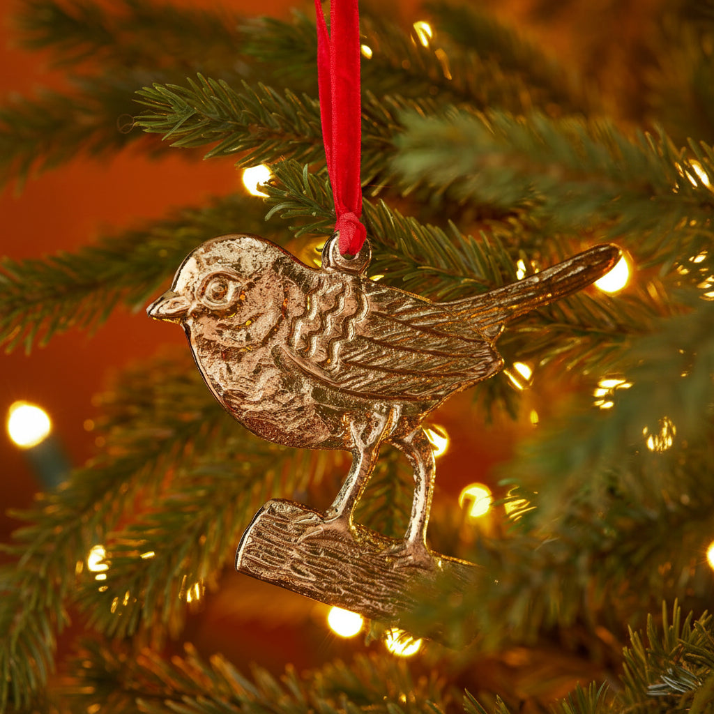 A metallic bird Christmas ornament hanging from a red ribbon on a decorated Christmas tree with warm lights.
