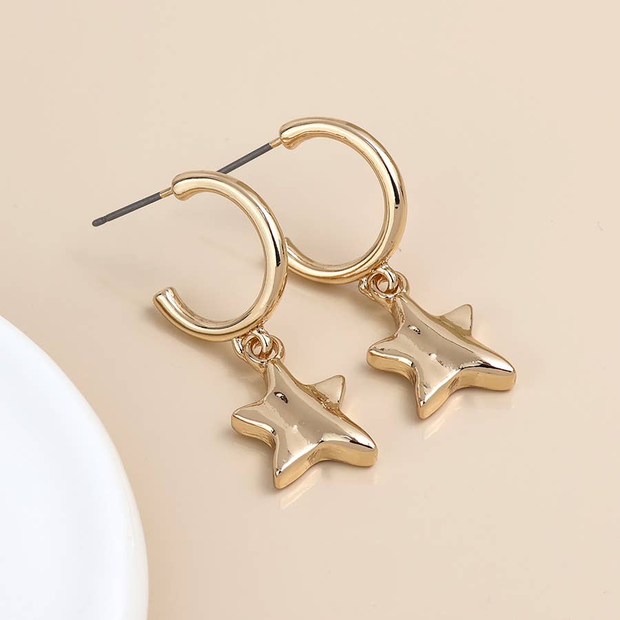 Gold open hoop star charm earrings hanging from a white dish edge
