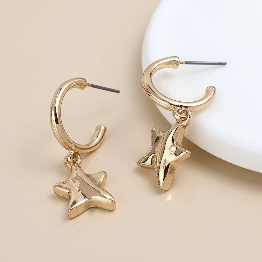 Gold C hoop earrings with wavy star charms beside a white dish on cream