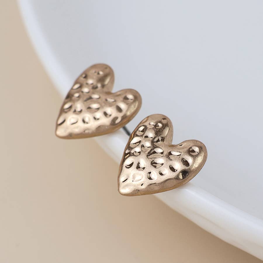 Pair of hammered gold heart studs on a white dish