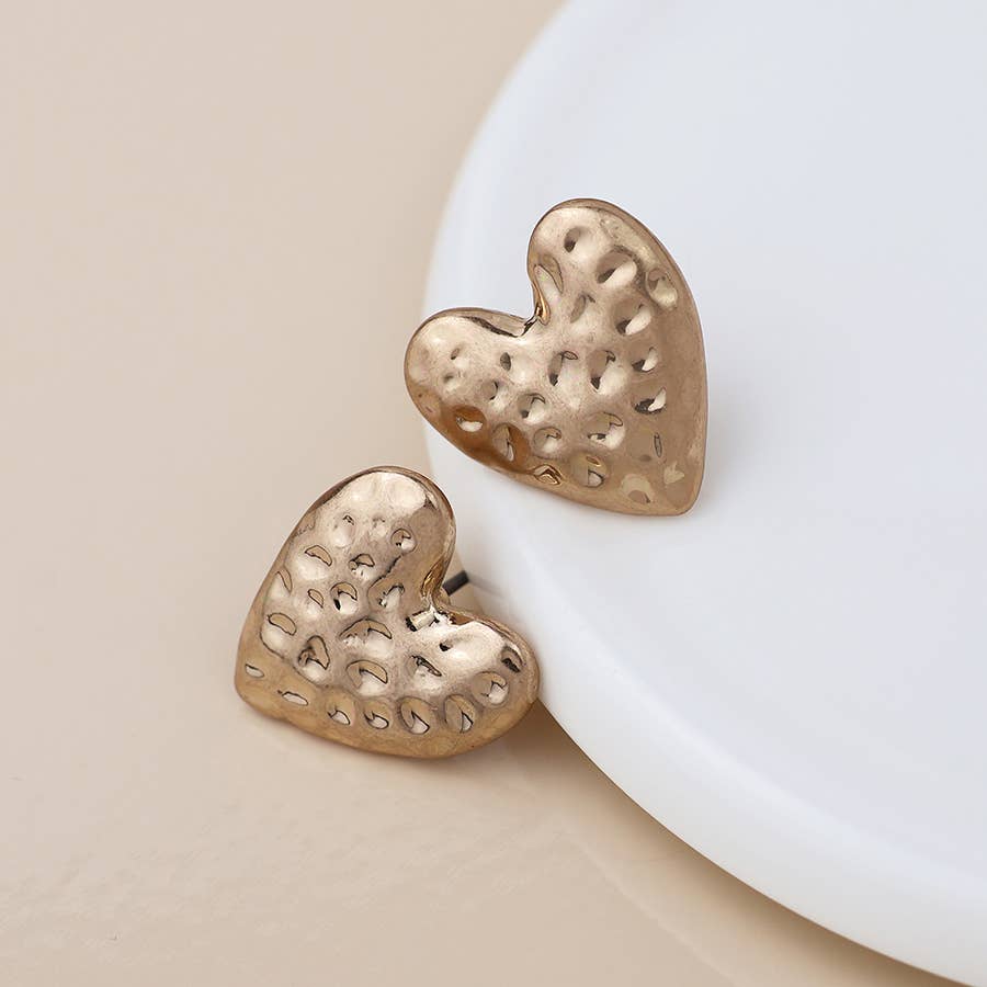 Hammered gold heart stud earrings leaning on a white dish, cream background