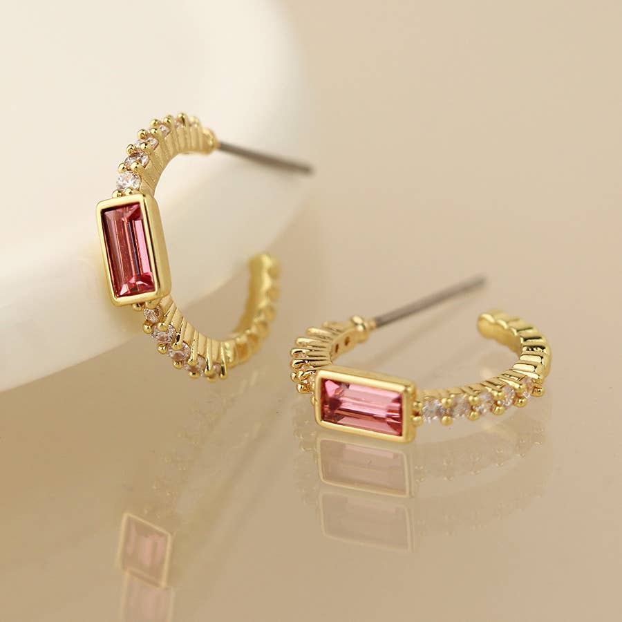 Gold hoop stud earrings with pink and clear crystals on a cream surface