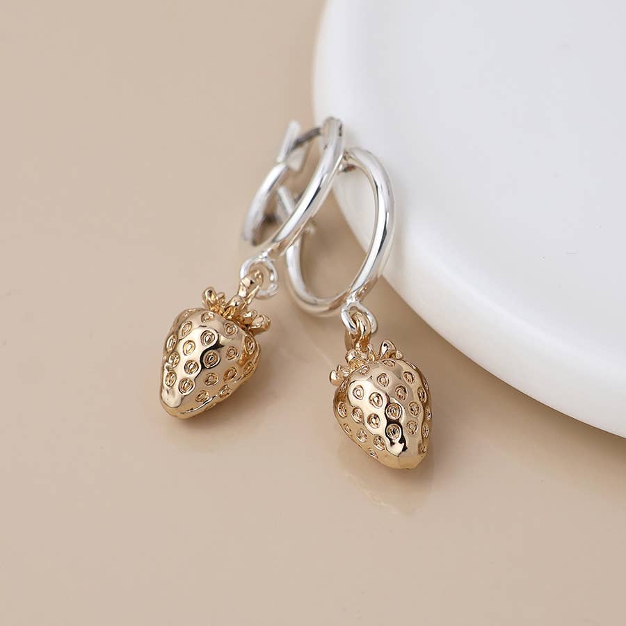 Silver hoop gold strawberry earrings hanging from a white dish