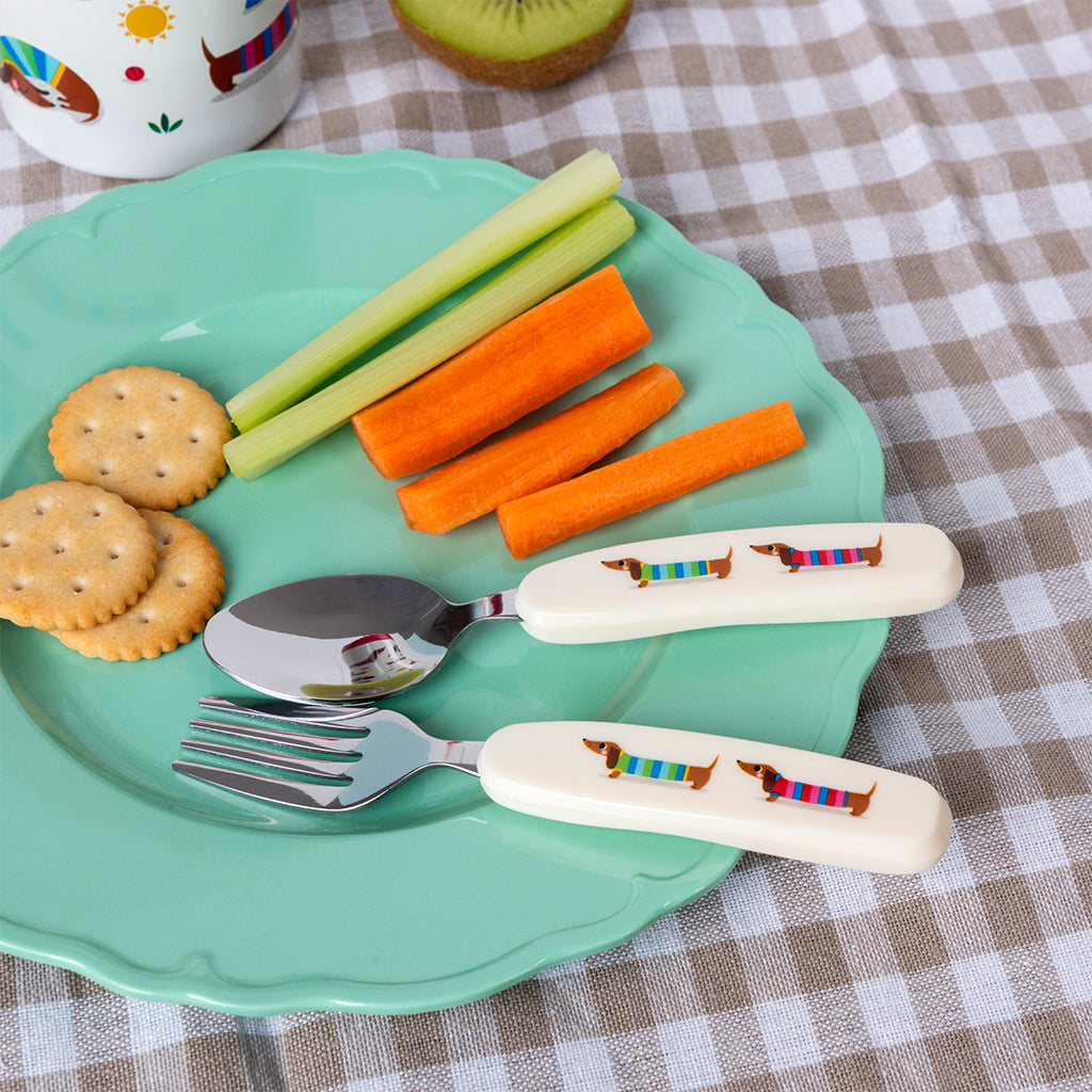 Sausage dog fork and spoon on a green plate of crackers, carrots and celery