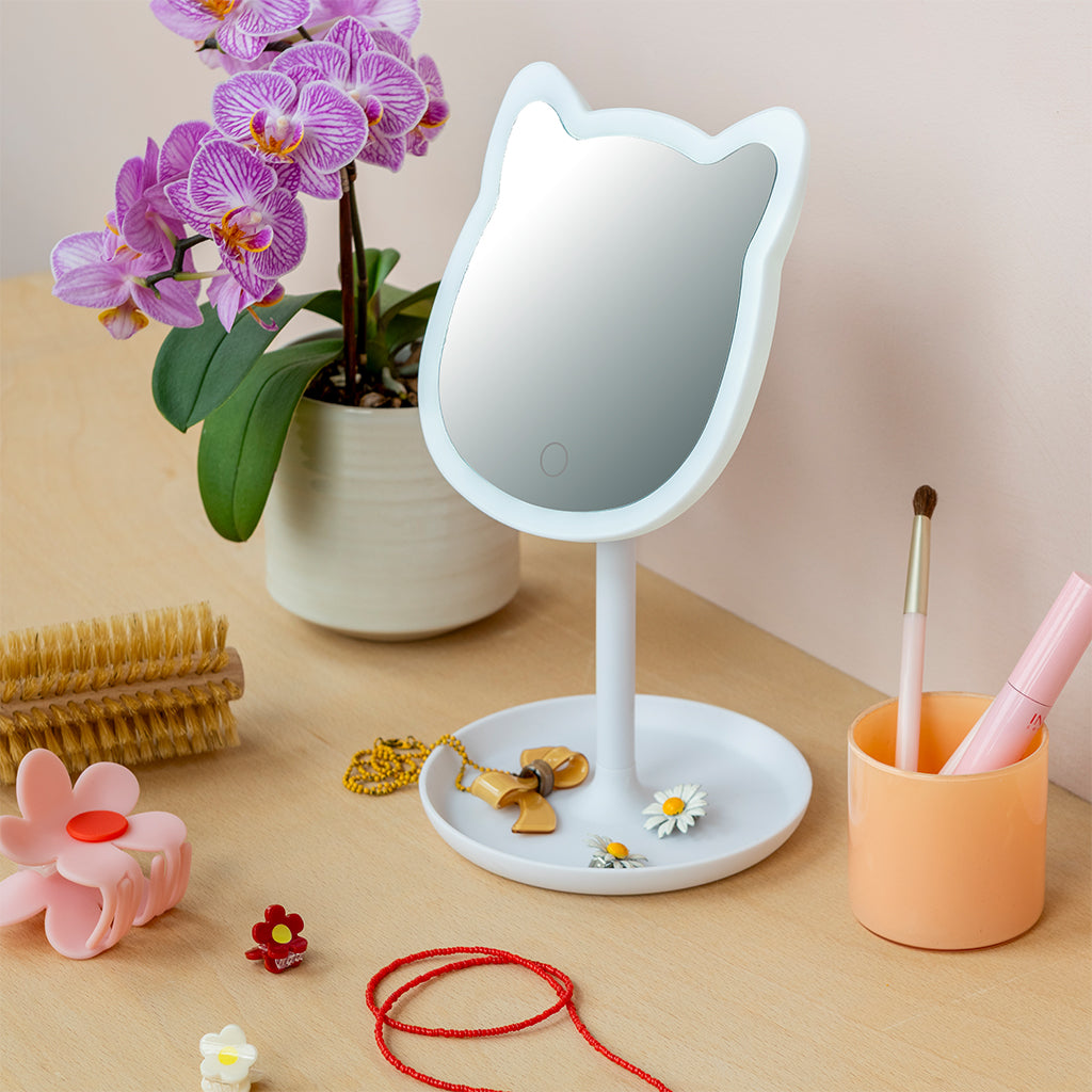 Cat vanity mirror on a dressing table beside an orchid and make-up brushes