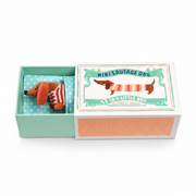 Mini sausage dog soft toy in a stripy jumper inside its opened illustrated gift box
