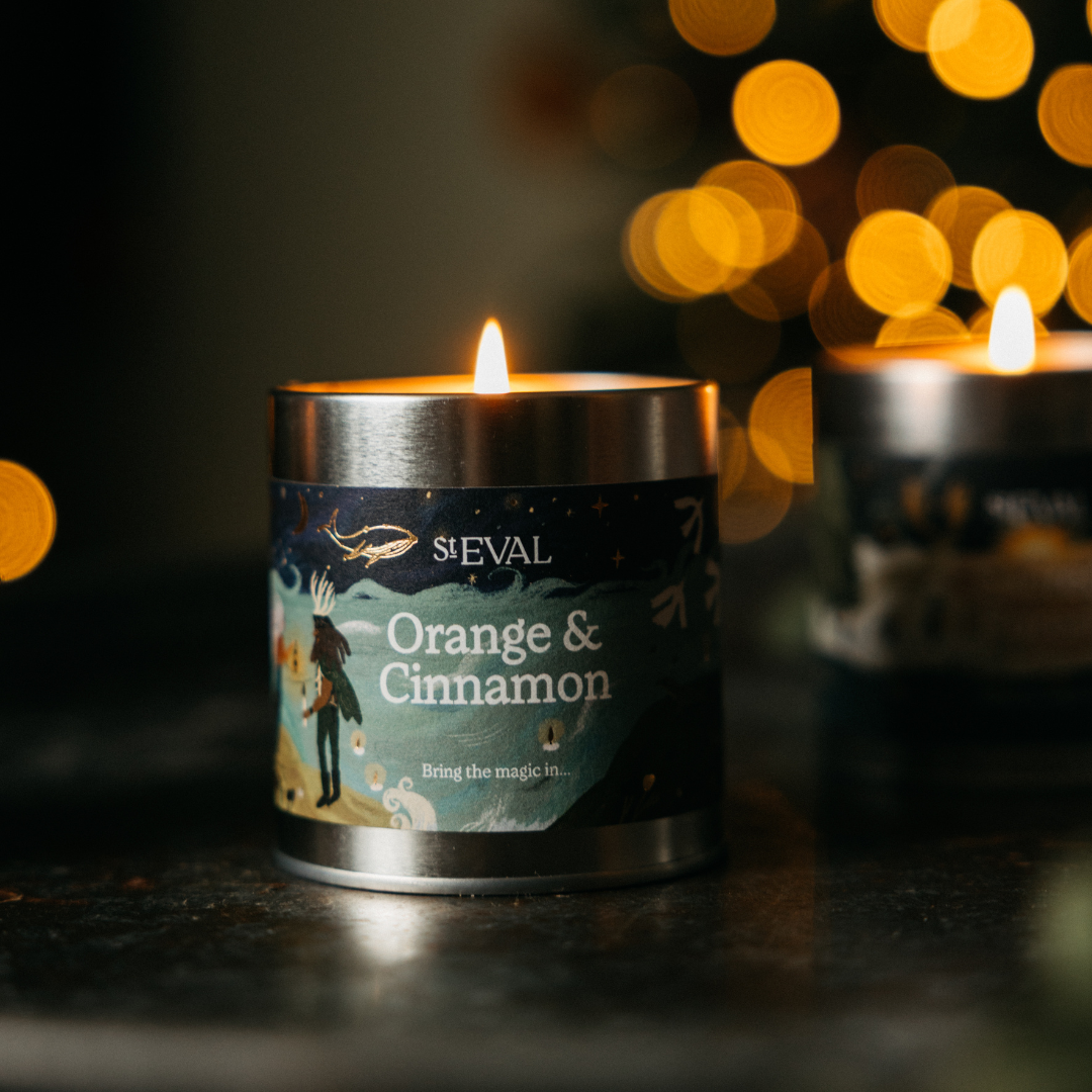 Orange & Cinnamon Christmas Tin Candle lit on a dark table with festive lights behind