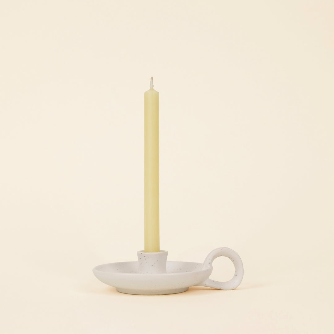 White Speckle Mini Candle Holder with Handle holding an ivory mini candle, cream background