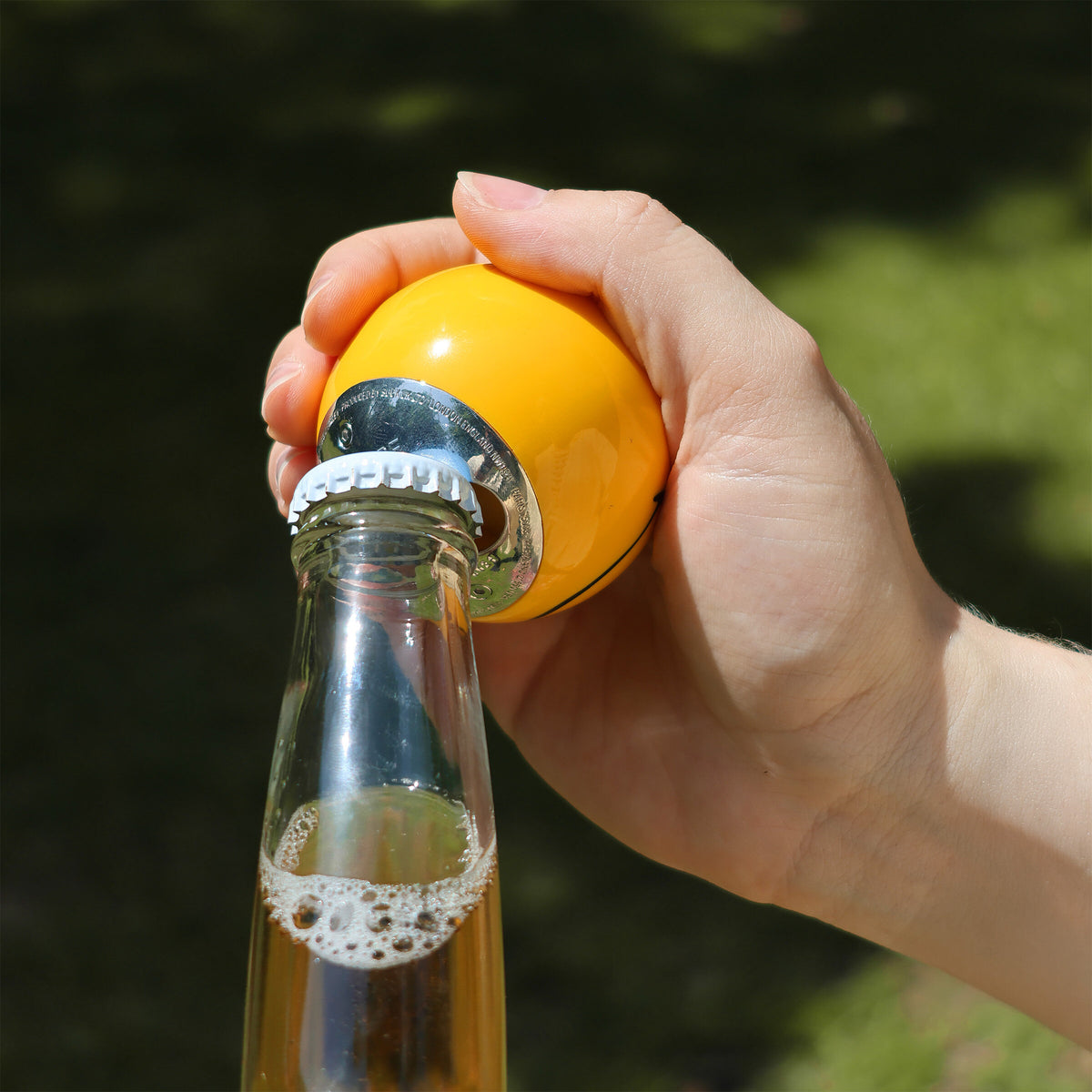 Smiley bottle opener popping the cap off a bottle outdoors on grass